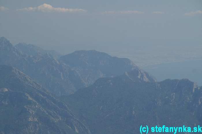 Kuk teleobjektívom smerom na Beldibi a Antalyu. Beldibi ležalo za tým masívom ležiacim približne nad stredom fotkx. Antalya je tá beloba mierne viditeľná za pravým okrajom spomínaného masívu.  Pozn.: Tie biele kopčeky hore sú mraky