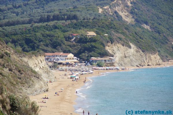 Ešte jeden pohľad z vyhliadky pred Agios Georgios south. Budova úplne vpravo pri mori je nefunkčná taverna na útese v Santa Barbare. Barák vľavo od nej je supermarket pri pláži (aj s tavernou prirodzene), poza supermarket viac do ľava ide asfaltka k odbočke na Corfu trail (a ďalšiemu supermarketu).  Corfu trail je ten chodník v pravej hornej časti obrazu a orientačne náročnejší variant chodníka vedie popod ten pás tmavých stromov zľava, smerom doprava, ku chodníku