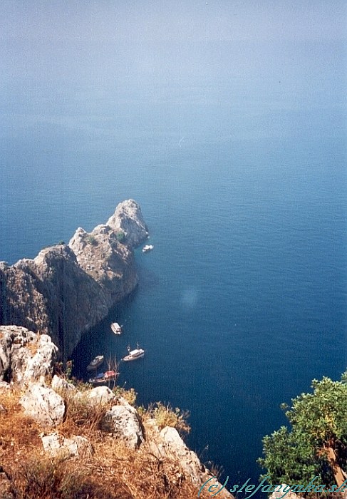 Alanya, Fosforeskujúca jaskyňa. Pohľad z hradu Alanyia. Kotviace lode vyzdvihujú odvážlivcov, ktorí prešli Jaskyňu lásky (cez ten výbežok) a skočili do mora. Spomínaná Fosforeskujúca jaskyňa sa nachádza niekde v pravom dolnom rohu 