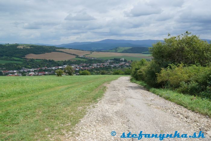 Bošáca a v pozadí Inovec (a pohorie Považský Inovec). Medzi nimi (spojnica kostol-Inovec) je taký nevýrazný kopček s lichobežníkovou svetlozelenou lúkou. Na jej hornom ľavom kraji je vyhliadka Hájnica